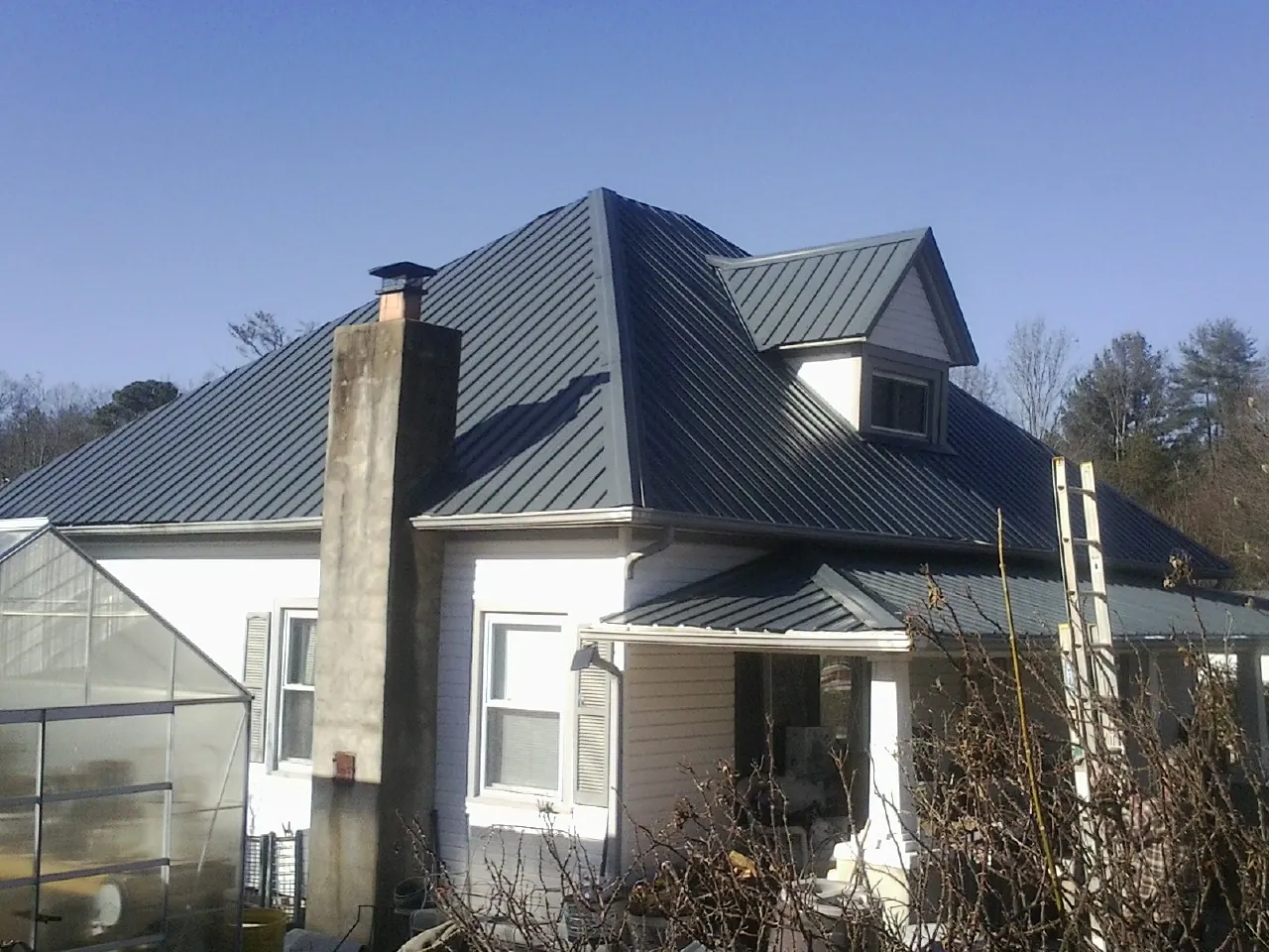 Dark blue standing seam metal roof on a white farmhouse with dormer — Slate & Tile Roof Repair by Roofing Brothers in Fort Riley