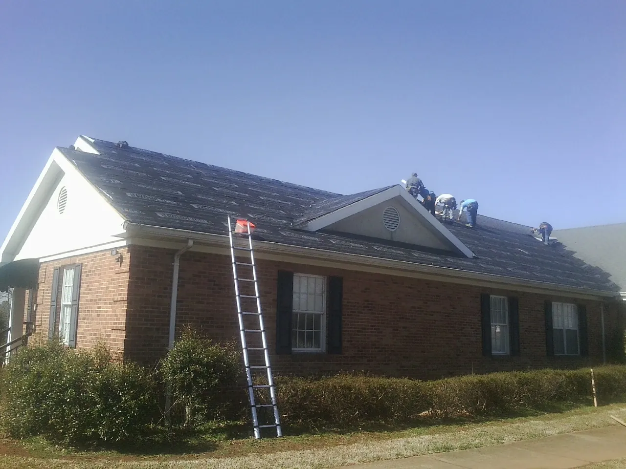Crew tearing shingles off a brick ranch roof with a ladder set — Metal Roof Repair work by our crew in Fort Riley