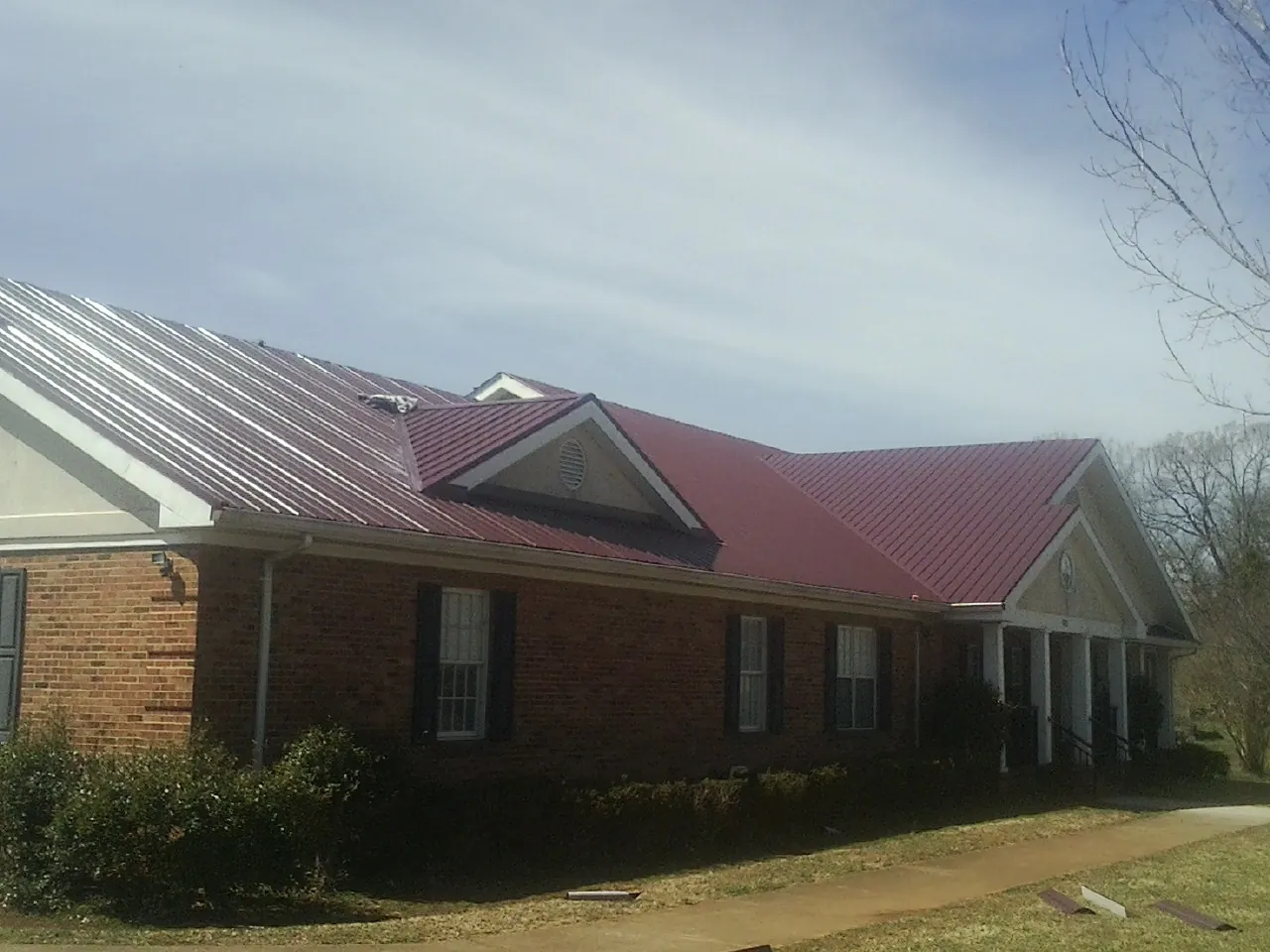 Red metal roof with gabled entries on a long brick building, from a Hail Damage Roof Repair job in Fort Riley
