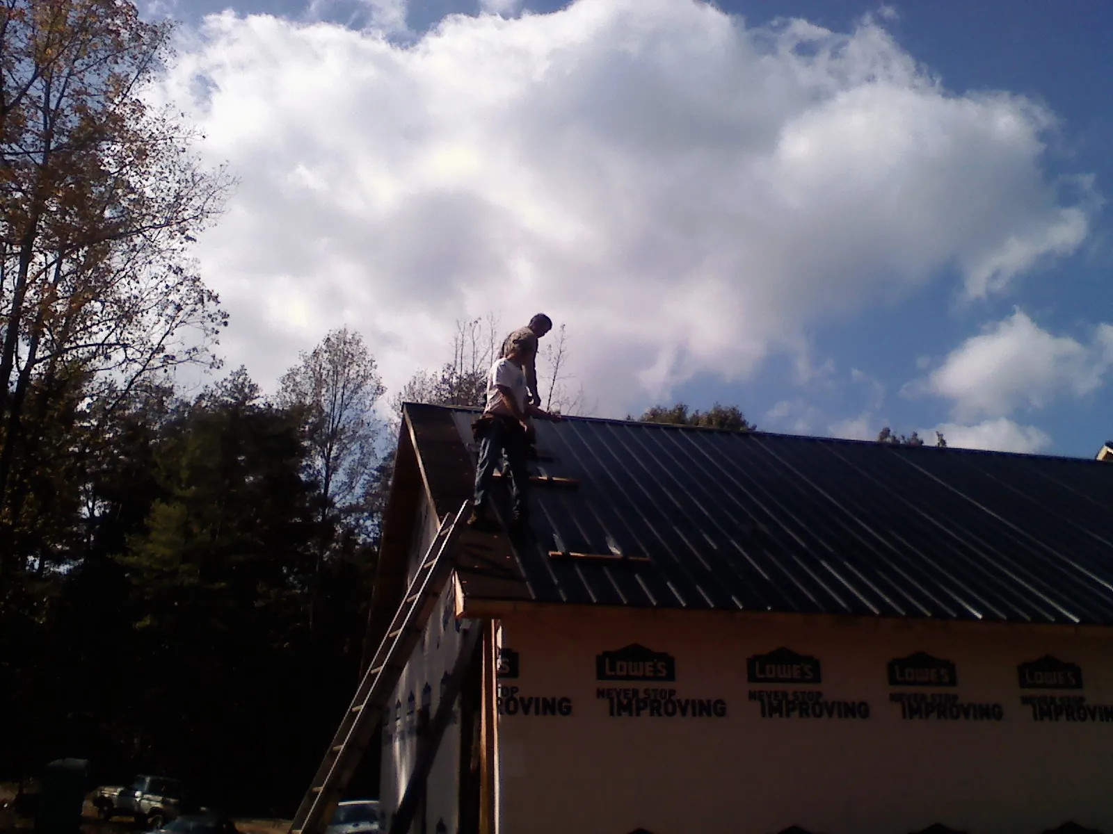 Roofer fastening dark metal panels high against a cloudy sky, from a Roof Inspection job in Fort Riley