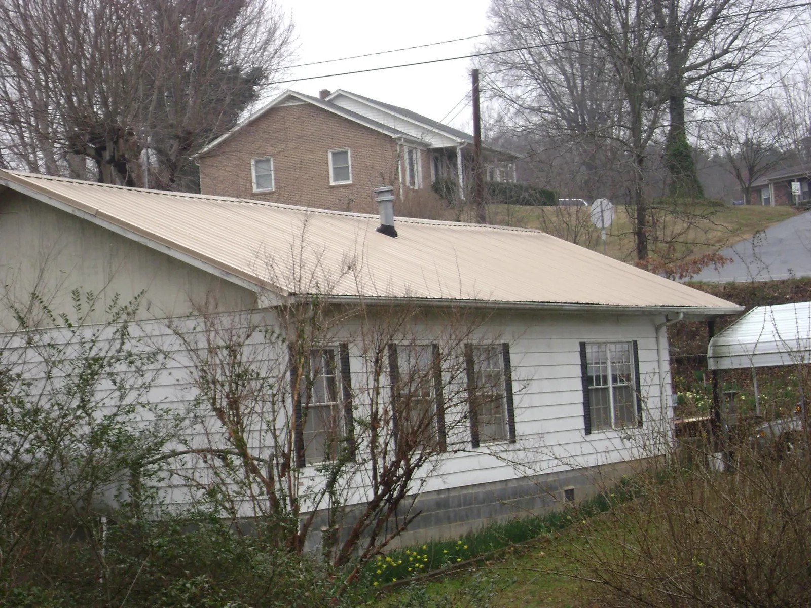 Tan metal roof on a white sided house set into a hillside — Commercial Roofing by Roofing Brothers in Fort Riley
